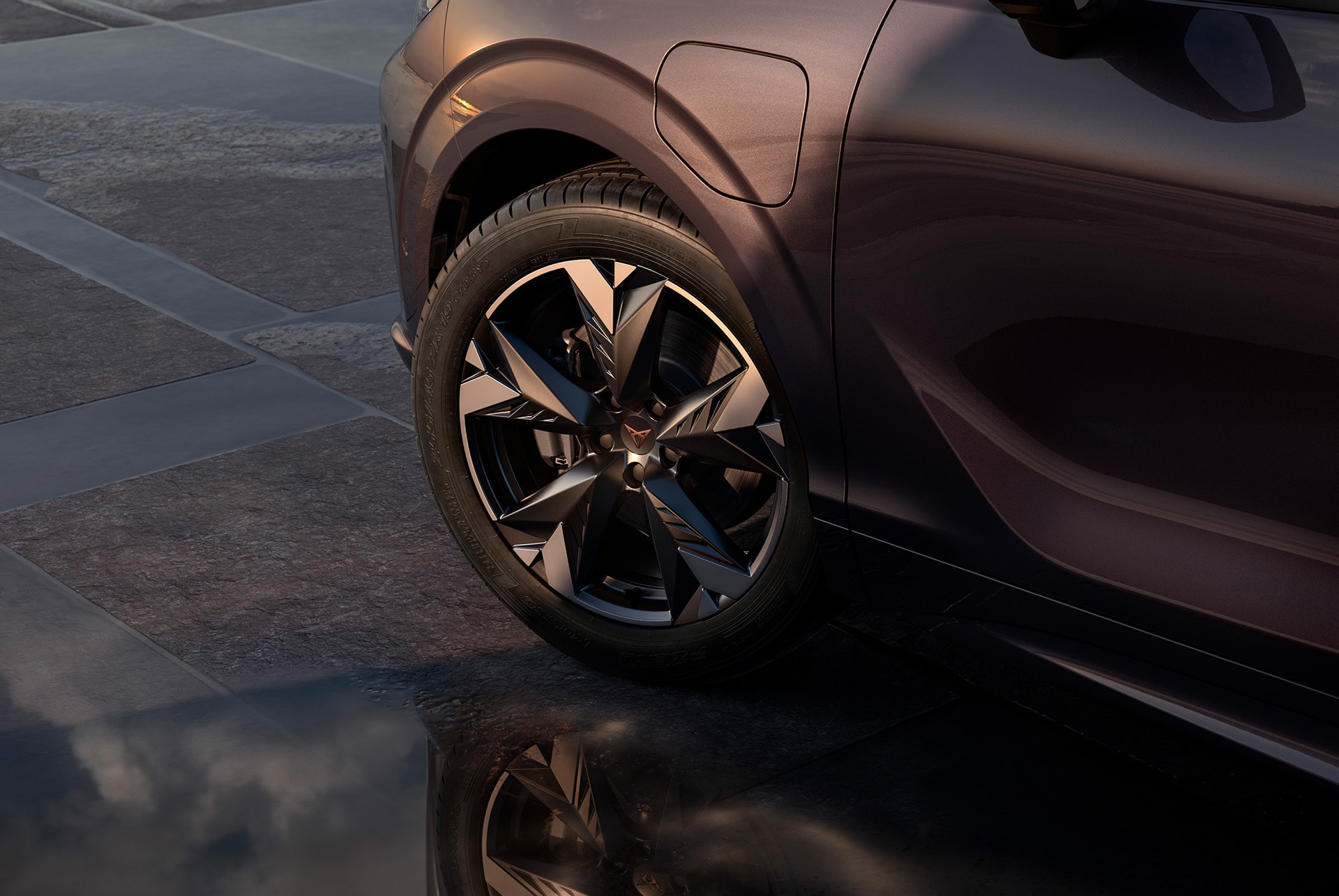 20 inch hadron copper alloy wheel on the new cupra terramar, in black with copper accents. Background includes a tiled pavement and part of the car's glossy, dark body.